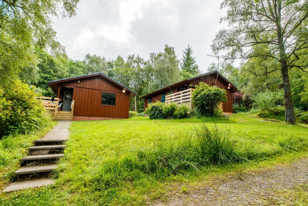 a cabin in the woods with a grass yard at Firbush Lochside Lodges in Killin