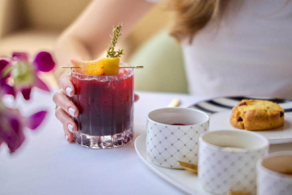 A close-up tea-and-drinks table with cups, a pastry and a garnished red cocktail.