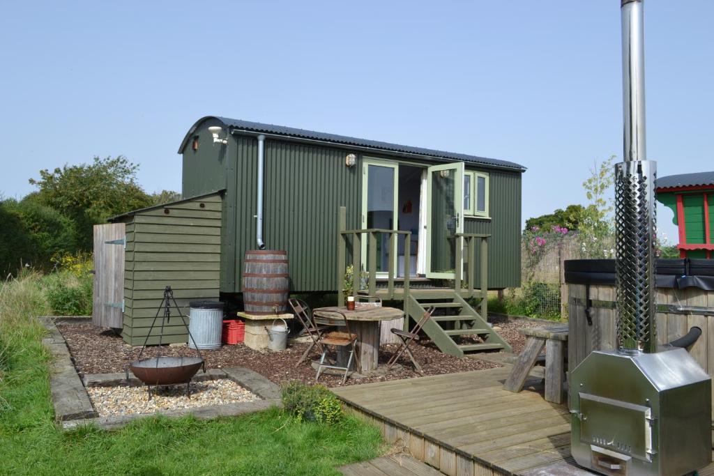 a green tiny house in a yard with a wooden deck at Twin Barn Shepherd’s Huts in Norwich