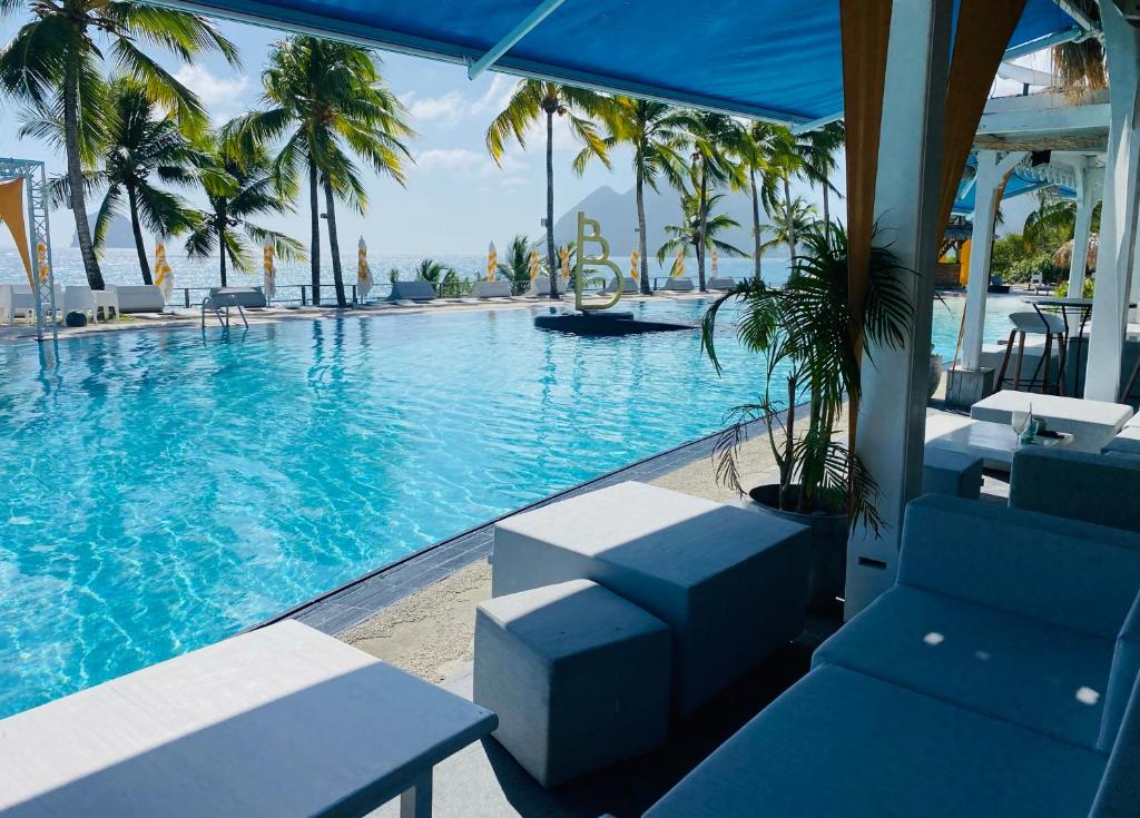 a swimming pool with blue chairs and palm trees at Diadora au magnifique panorama - Studio neuf de prestige vue mer in Le Diamant