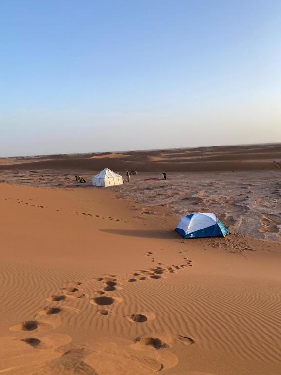 two tents in the desert with footprints in the sand at Sahara Camp Light in Mhamid