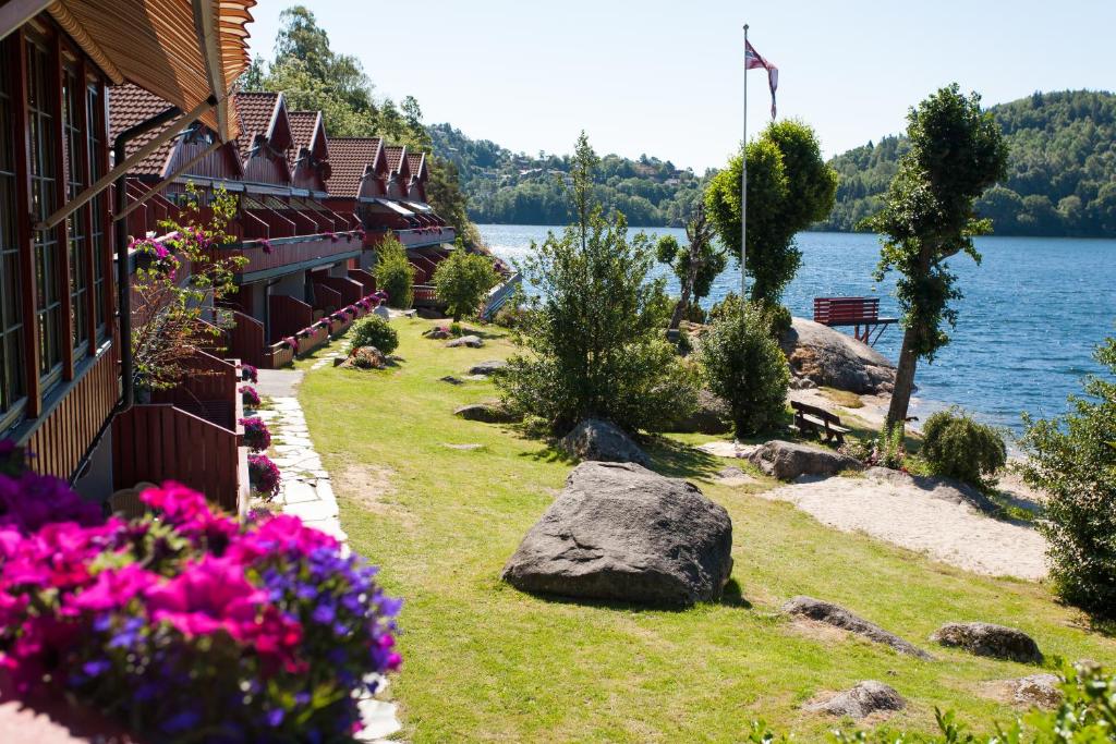 a building on the shore of a lake with flowers at Mones Feriesenter in Mandal