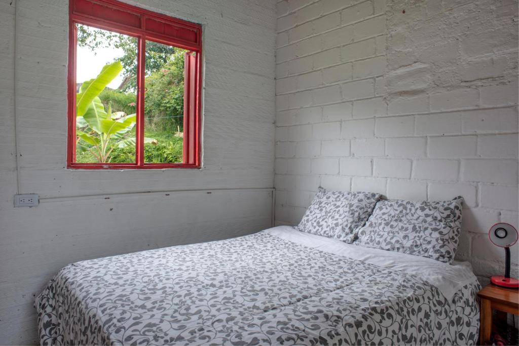 Cama en habitación blanca con ventana en Hacienda Venecia Hostel en Manizales