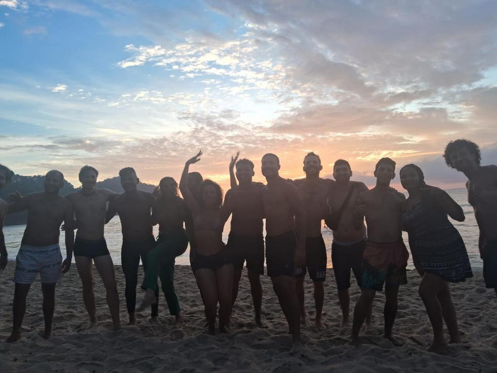 Un grupo de personas de pie en la playa al atardecer en Efferus Hostel, en Ubatuba