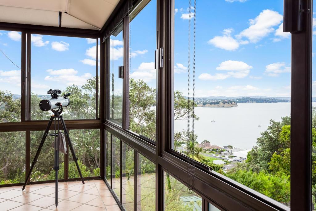 une caméra sur un tripod dans une chambre avec fenêtres dans l'établissement Harbour Retreat with sea views and BBQ, à Whangaparaoa