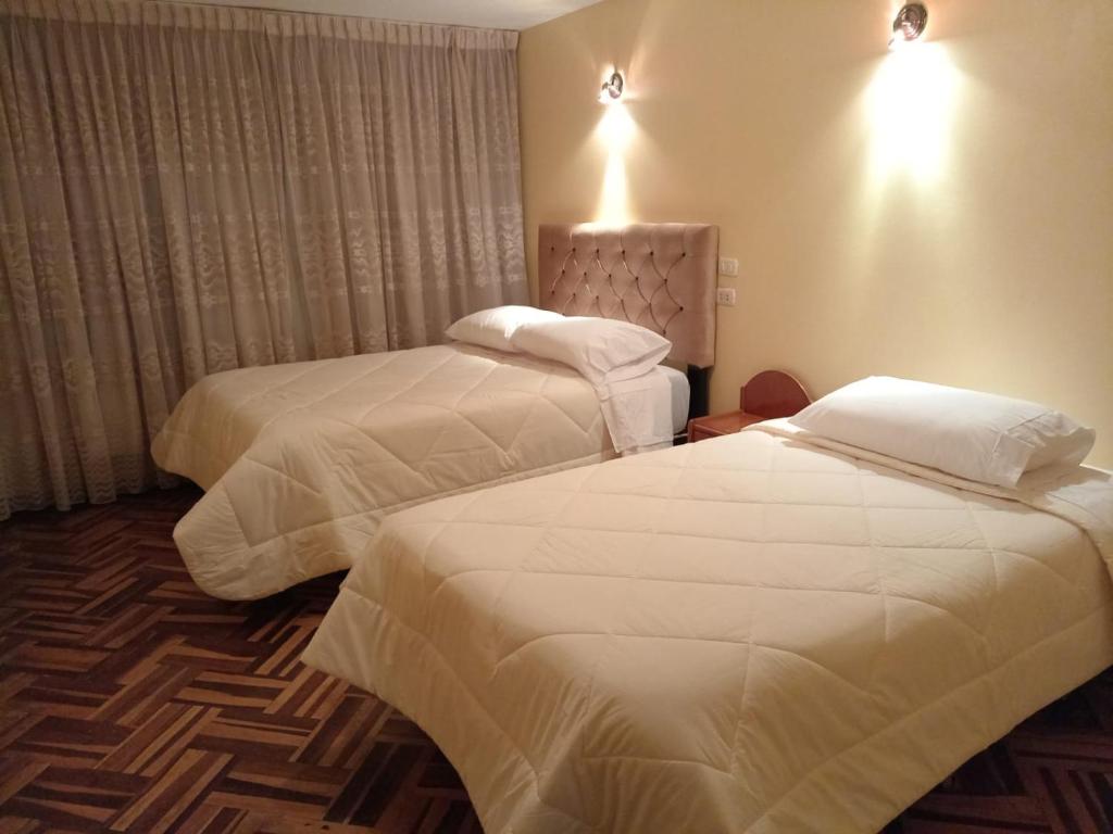 duas camas num quarto de hotel com lençóis brancos em HOSTAL SUIT ANDINA em Puno