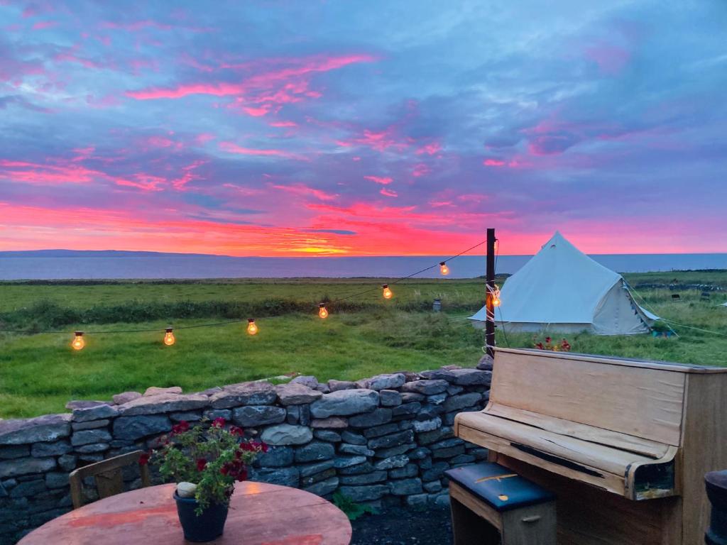 a sunset with a tent and a table and a bench at Glór na d'Tonnta Glamping in Sligo
