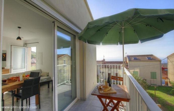 - un balcon avec une table et un parasol vert dans l'établissement Idéal logement Cargese 4, à Cargèse