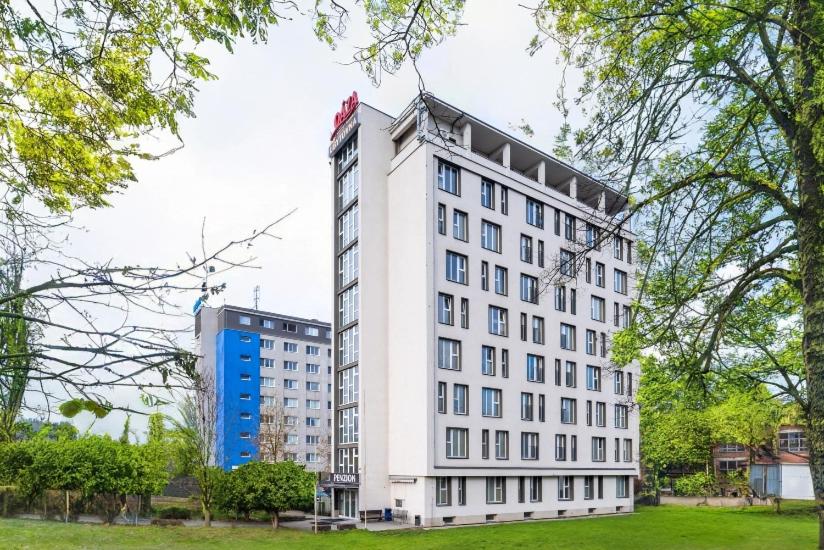 a tall white building in a park with trees at Penzion a ubytovna Oáza in Otrokovice