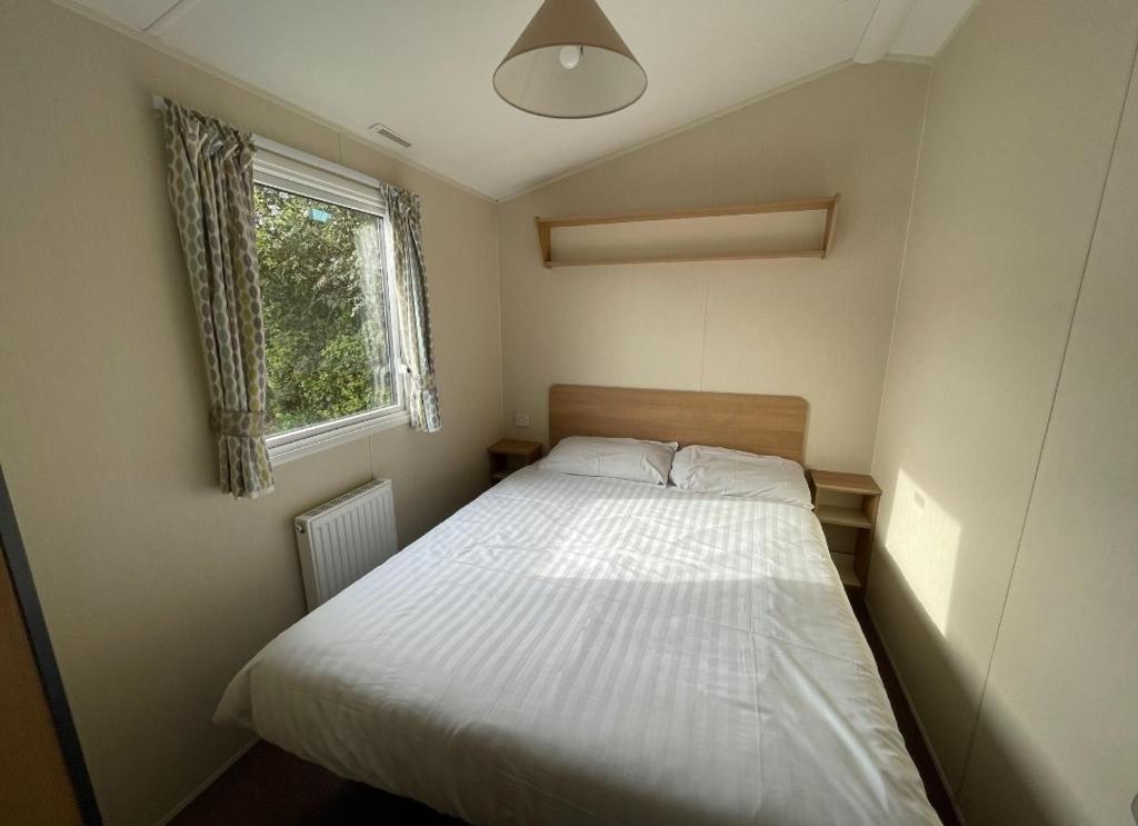 a small bedroom with a white bed and a window at Sycamore Caravan in Helston