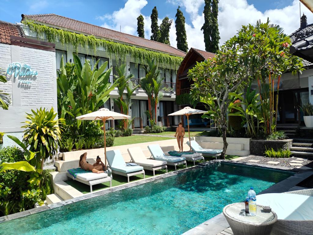 a pool with lounge chairs and umbrellas next to a building at The Palms Canggu in Canggu