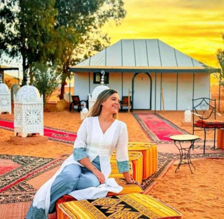 una mujer sentada en una mesa frente a un edificio en Merzouga Luxurious Camp, en Merzouga