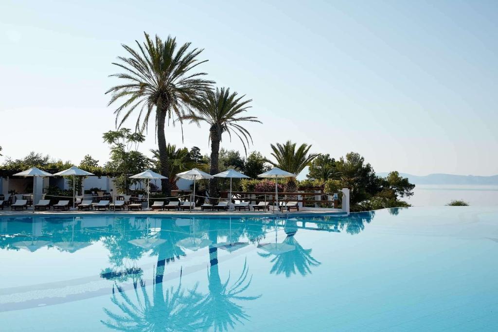 - une piscine avec des chaises, des parasols et des palmiers dans l'établissement Barceló Hydra Beach, à Thermisía