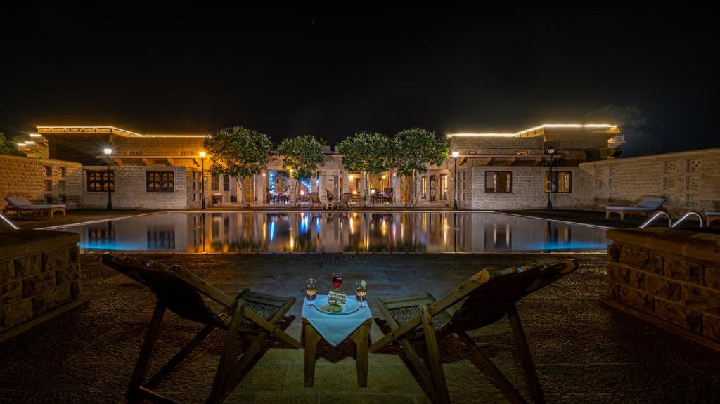 una mesa con 2 sillas junto a una piscina por la noche en Hotel Rawalkot Jaisalmer, en Jaisalmer