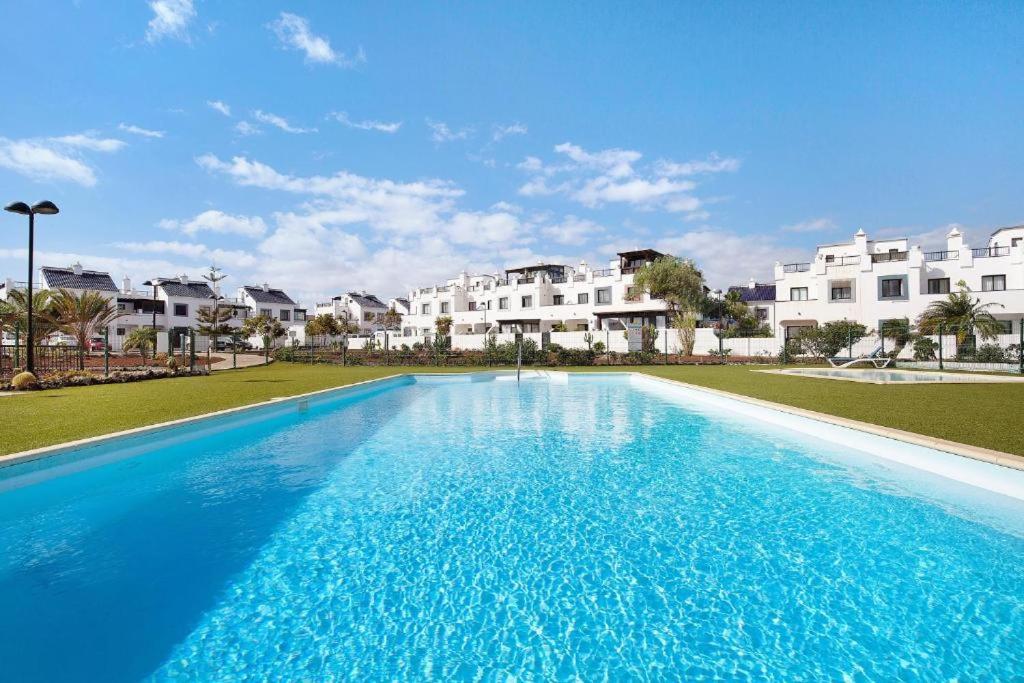 a large blue swimming pool with houses in the background at La Casa Blanca in Corralejo