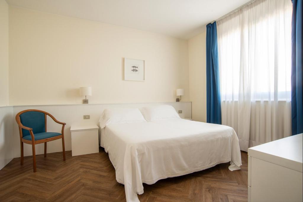 a white bedroom with a bed and a blue chair at Residence Atlantico in Lido di Jesolo