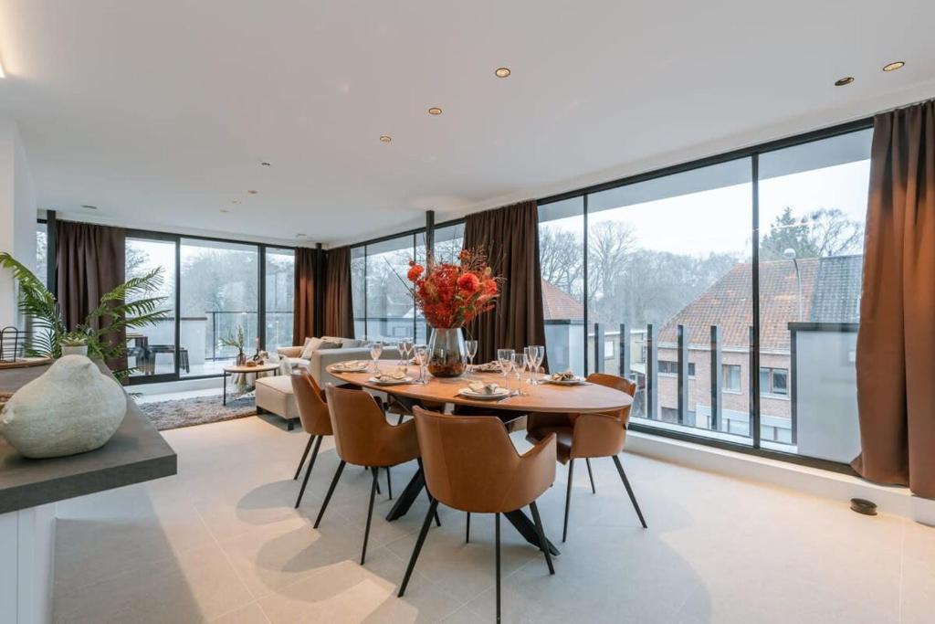 een eetkamer met een tafel en stoelen en grote ramen bij Apartment with two large terraces in Zedelgem