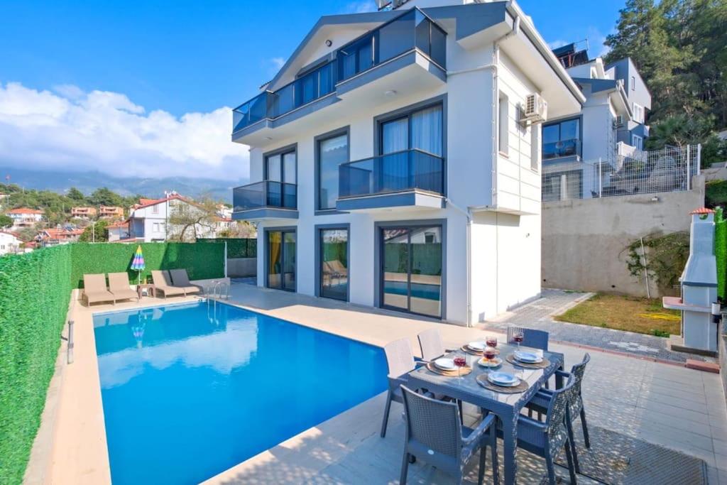 a house with a swimming pool and a table and chairs at Villa Simge 4+1 Ölüdeniz in Fethiye