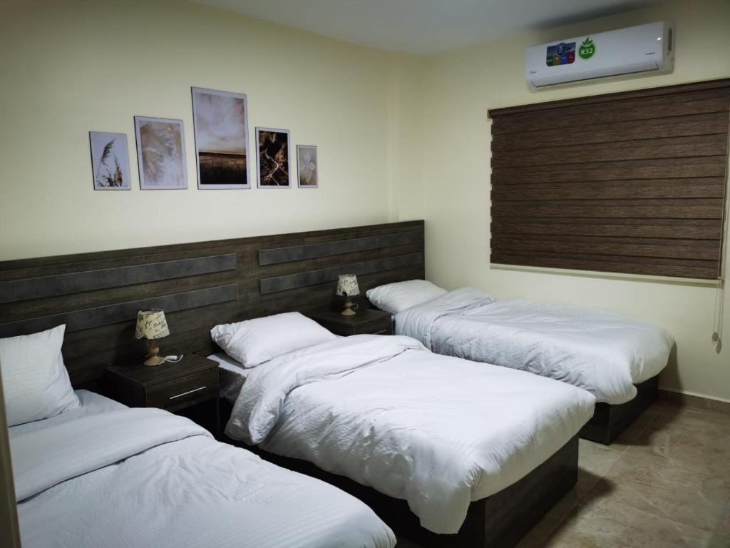 three beds in a room with white sheets at Hospitality apartments in Wadi Musa