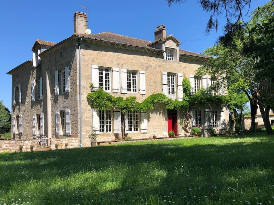 une ancienne maison en briques avec une porte rouge sur une pelouse dans l'établissement Grande maison en pierre de taille avec piscine, sauna et jacuzzi, à Madaillan
