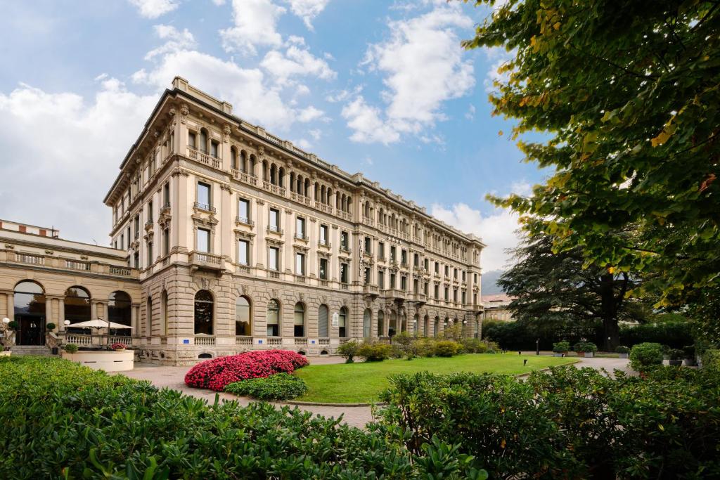 a large white building with a green park in front of it at Palace Hotel Lake Como in Como