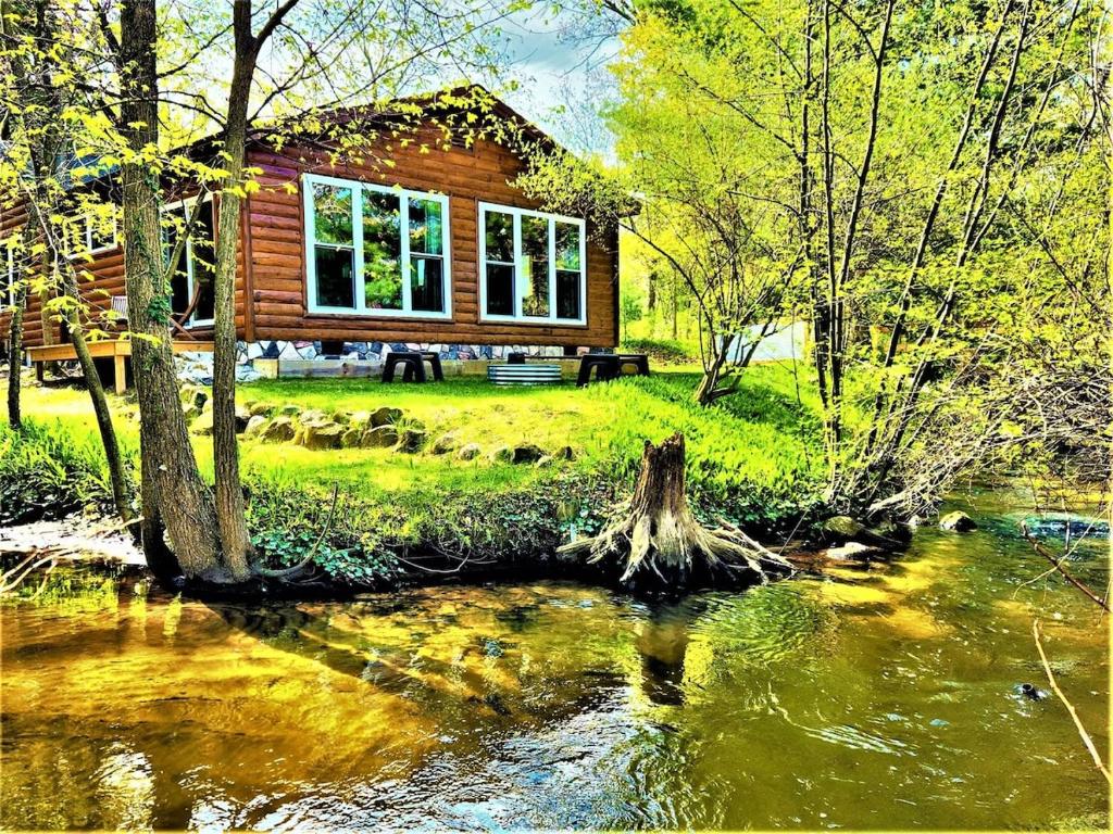 a log cabin next to a river with trees at Creekside Hot Tub-Walk to Beach-Uniquely Northern in Traverse City