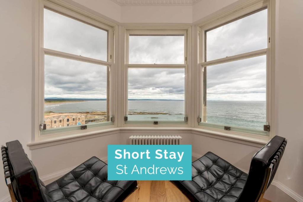 a room with two chairs and windows with a view of the ocean at Luxury Penthouse on The Scores - Best View in St Andrews in St Andrews