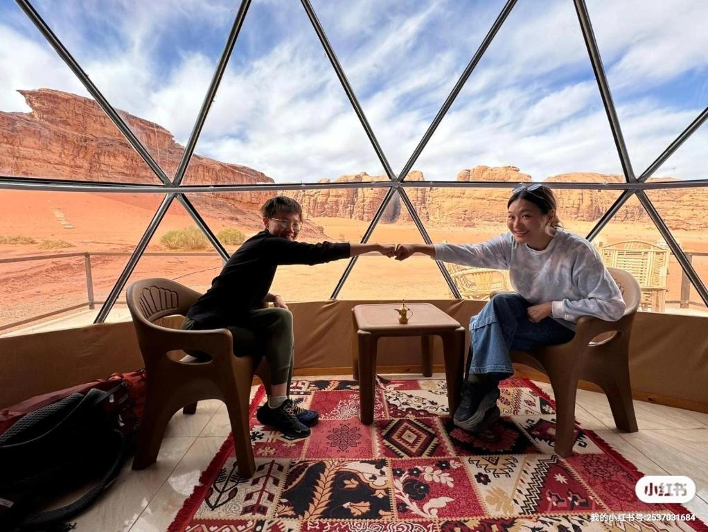 a man and a woman sitting in chairs in front of a window at Bubble RumCamp in Wadi Rum