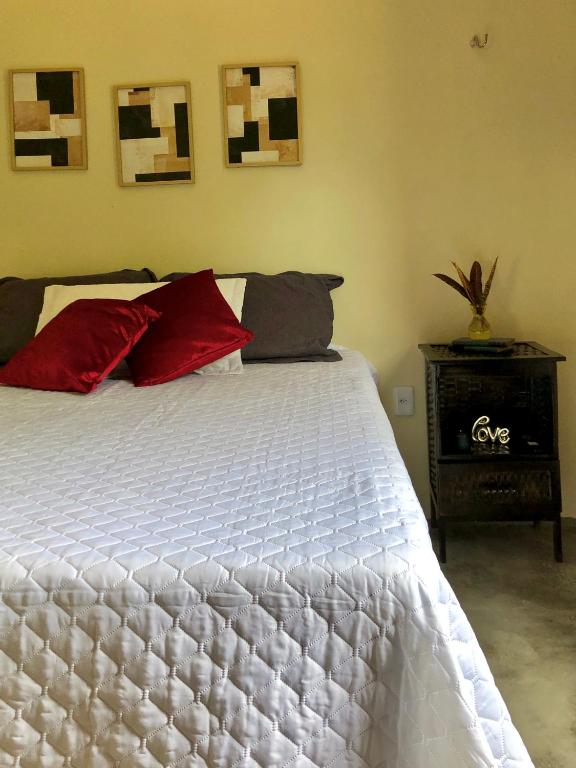 um quarto com uma cama branca e almofadas vermelhas em Sítio Primavera em Ipueiras
