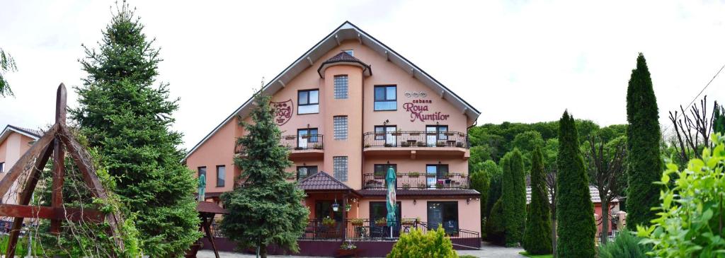 a large pink building with trees in front of it at Pensiunea Roua Muntilor in Vadul lui Carol II