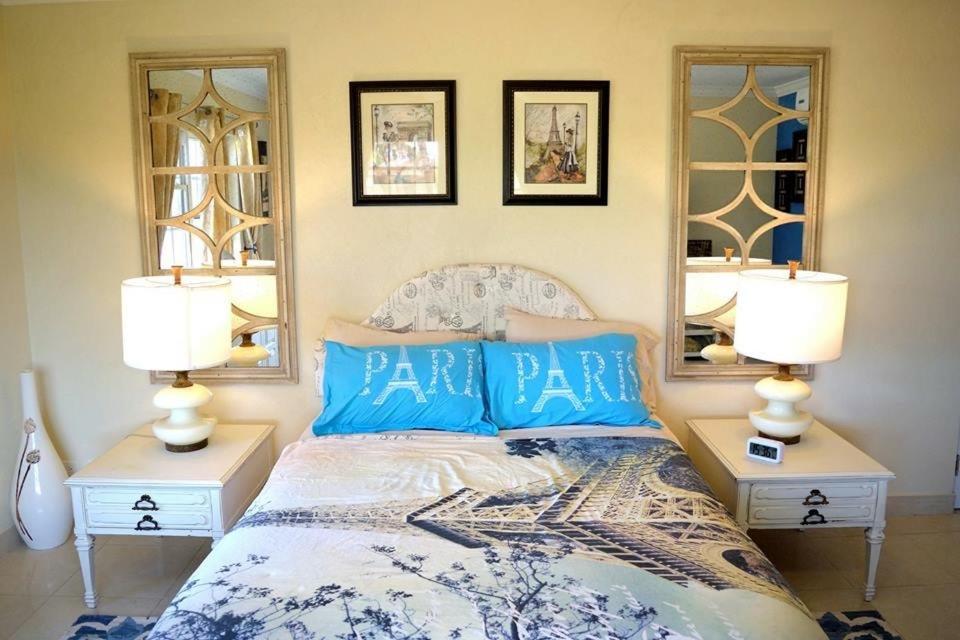 a bedroom with a bed with blue pillows and two lamps at Hidden Gem Barbados in Christ Church