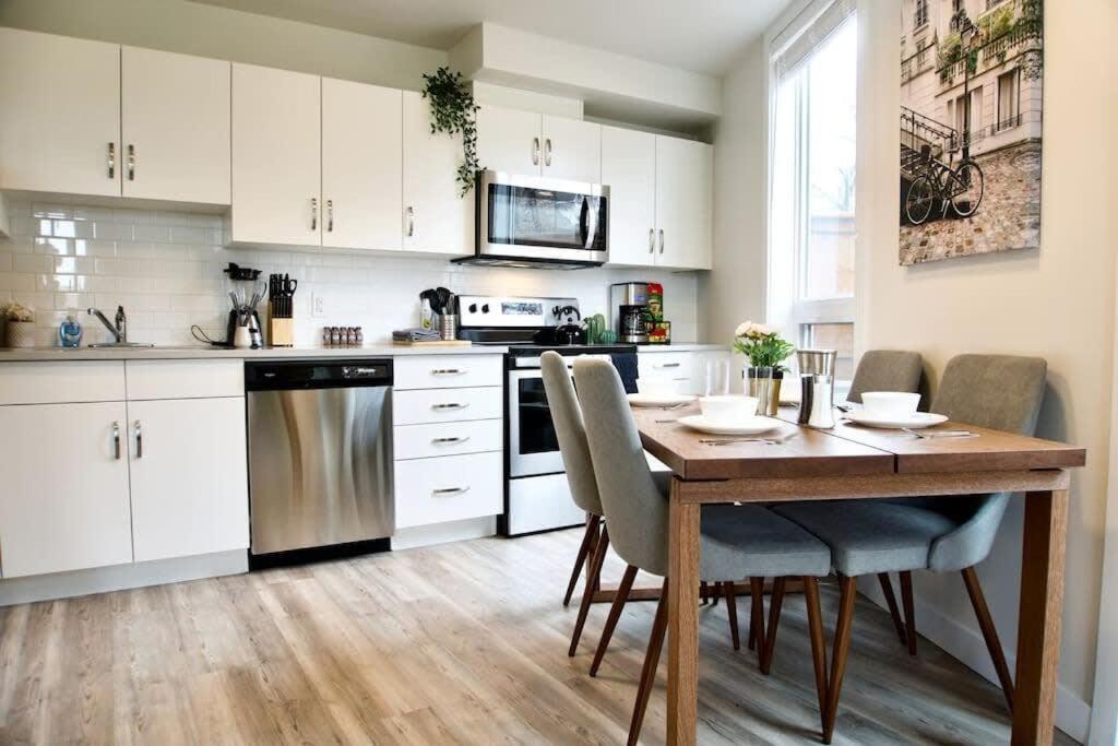 a kitchen with a wooden table and white cabinets at Gorgeous Modern 2BD Condo Heart of Wpg Coffee Location in Winnipeg
