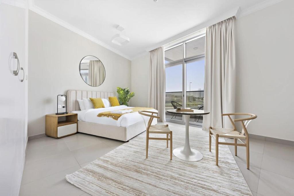 a white bedroom with a bed and a table and chairs at Silkhaus spacious studio in Art Gardens with gym & pool access in Dubai