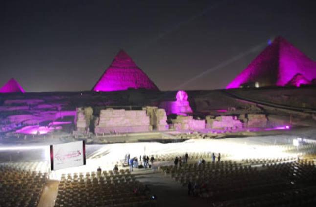 een groep mensen die 's nachts voor piramides staan bij Sphinx Pyramids Hotel in Caïro