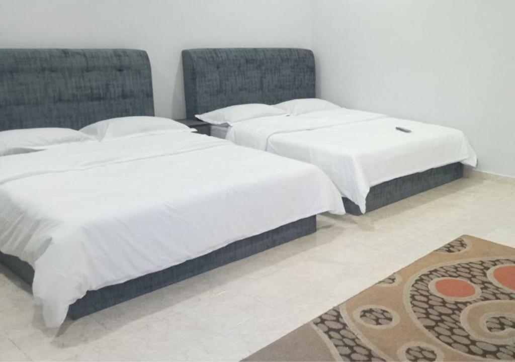 ドゥングンにあるAdamia Roomstay in Dungunのラグ付きの客室で、ベッド2台(白いシーツ付)