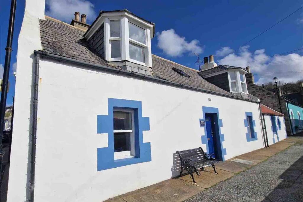 a white building with blue doors and a bench at Cullen Seaside Cottage in Cullen