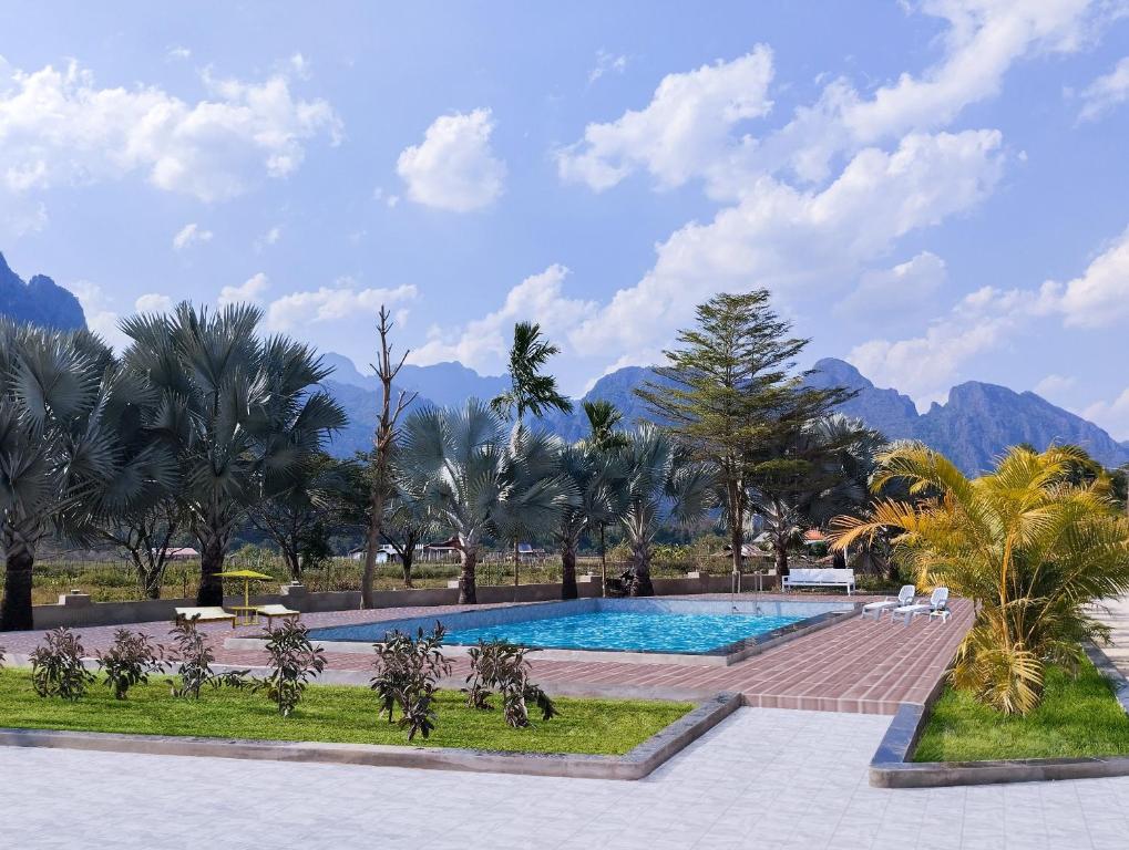 a swimming pool with palm trees and mountains in the background at Vang Vieng Romantic Place Resort in Vang Vieng