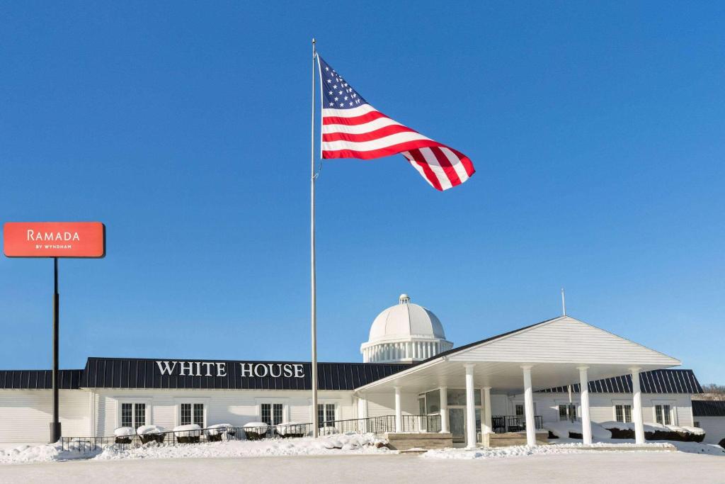 una bandera americana ondeando frente a una casa blanca en Ramada by Wyndham Richland Center, en Richland Center