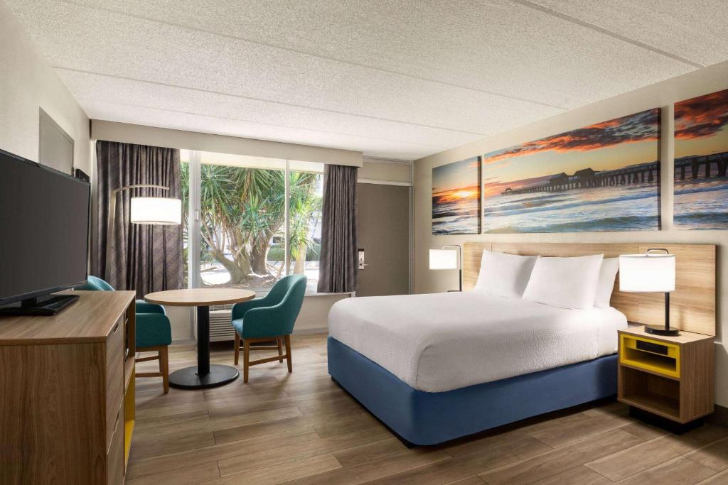 una camera d'albergo con letto, scrivania e tavolo di Days Inn by Wyndham Cocoa Beach Port Canaveral a Cocoa Beach