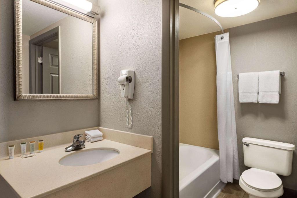 ein Badezimmer mit Waschbecken, Toilette und Spiegel in der Unterkunft Days Inn by Wyndham Cocoa Beach Port Canaveral in Cocoa Beach