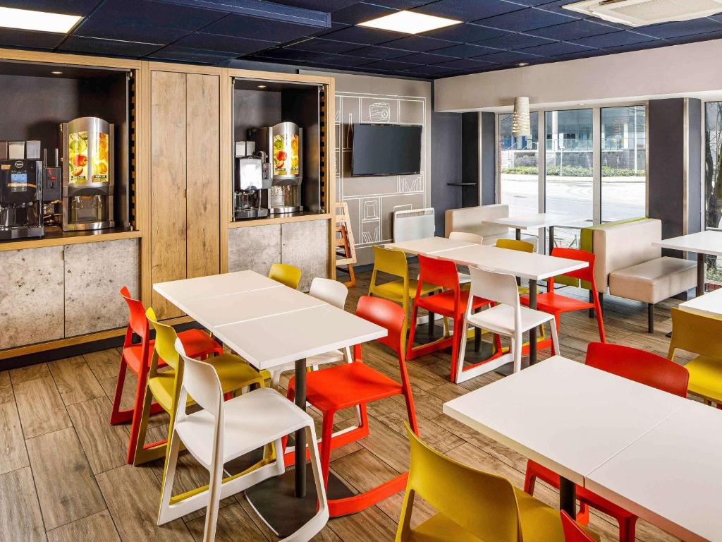 a restaurant with white tables and colorful chairs at ibis budget Cardiff Centre in Cardiff