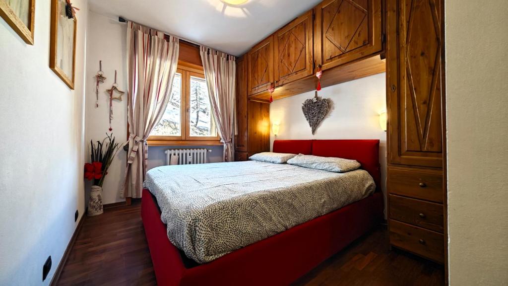 1 dormitorio con cama roja y armarios de madera en Hostdomus - Nebbiolo, en Sestriere