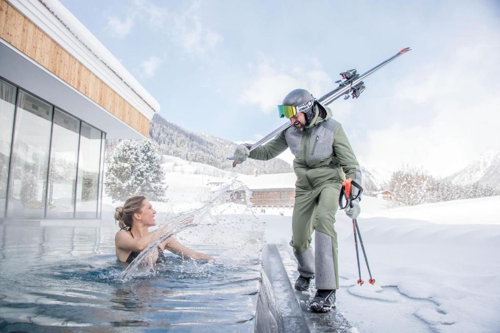 une femme dans une piscine avec un homme tenant des skis dans l'établissement Hotel Plunhof, à Ridanna
