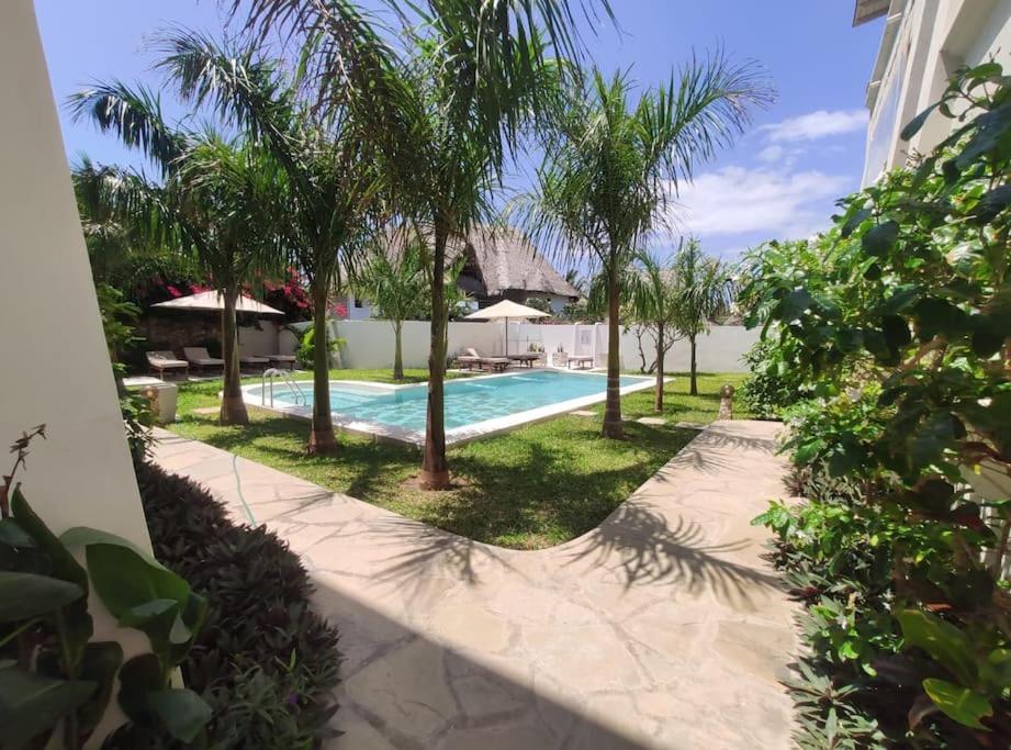 a swimming pool with palm trees next to a house at Apartment on the Sand in Watamu