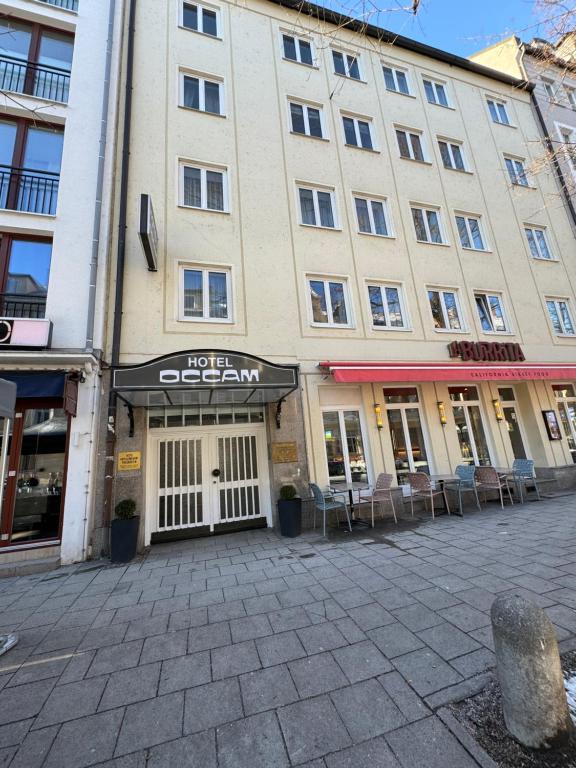 Hotel Occam في ميونخ: مبنى كبير امامه طاولات وكراسي