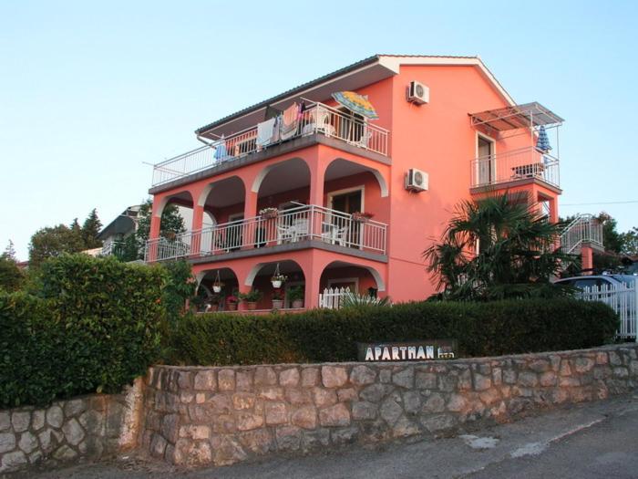 een groot roze gebouw met balkons aan een muur bij Apartmani Bura in Njivice