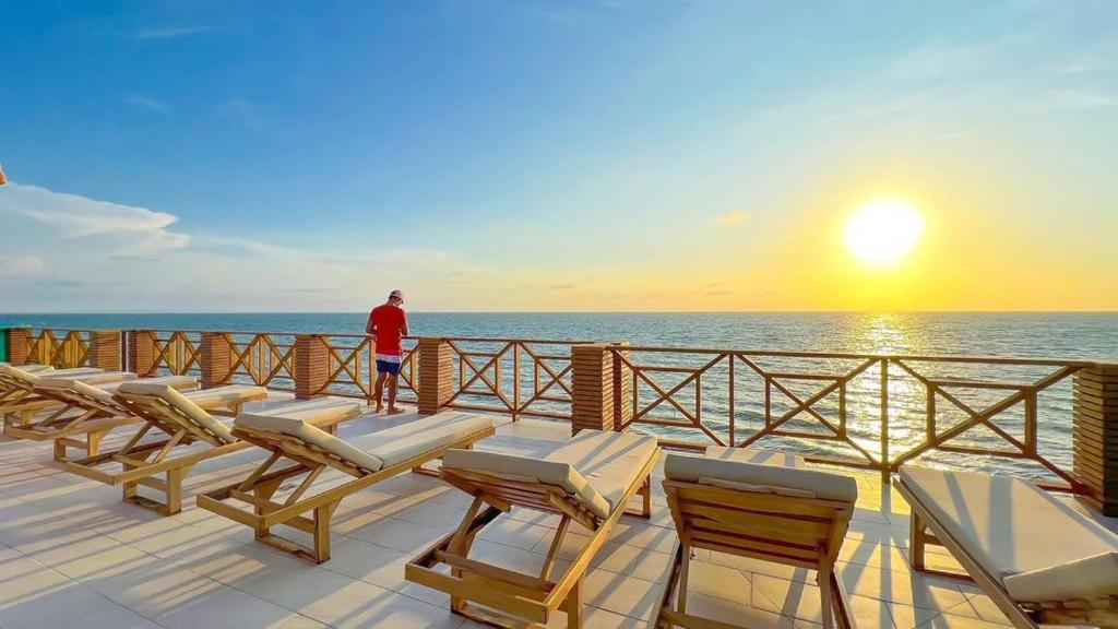 Ein Mann steht auf einem Deck und sieht den Sonnenuntergang. in der Unterkunft SUITE OCEAN VIEW - PLAYA in Tolú