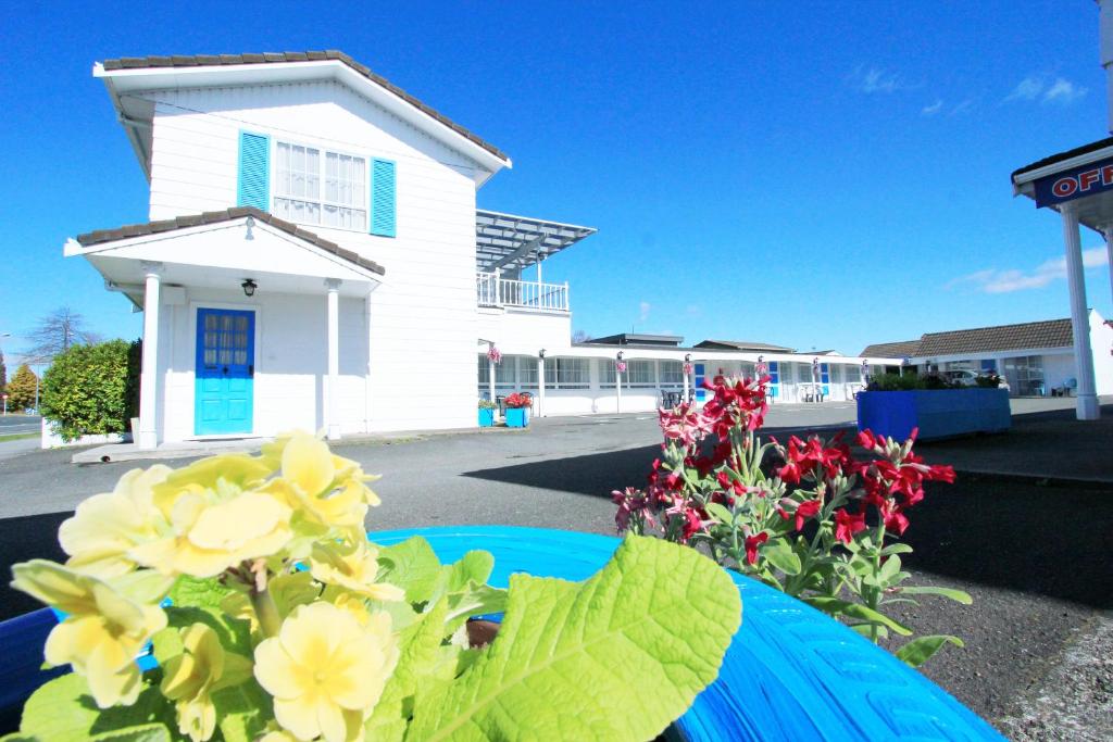 une maison blanche avec des fleurs devant elle dans l'établissement Golden Glow Motel, à Rotorua