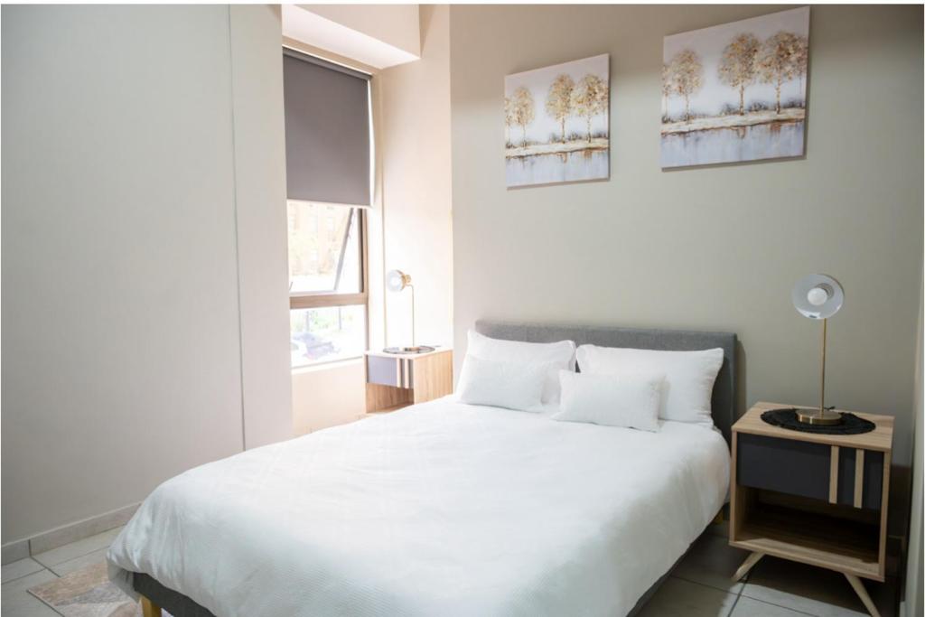 una camera da letto con un grande letto bianco e una finestra di The Bolton Rosebank Apartment 26 a Johannesburg