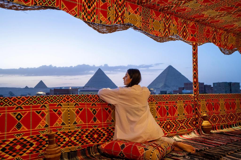 a woman sitting on a bench with pyramids in the background at king of pharaohs pyramids view in Cairo